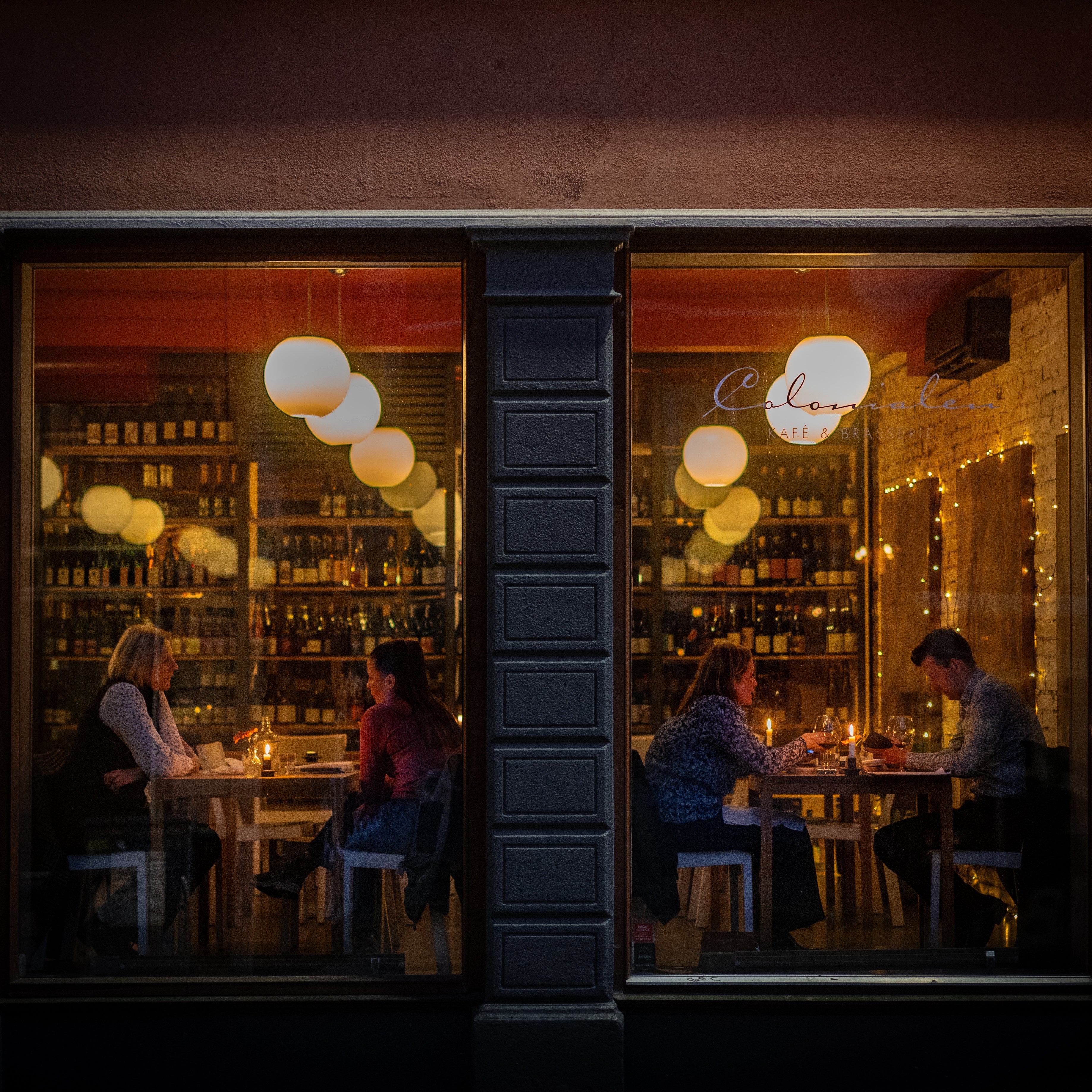 People enjoying a candlelit dinner inside a cozy restaurant in Bergen, Norway, viewed through large windows from the street at night.